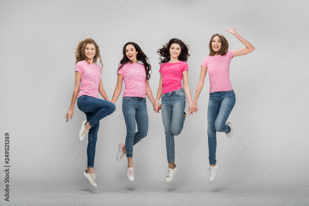 cheerful girls holding hands and jumping on grey background cheerful girls holding hands and jumping on grey background