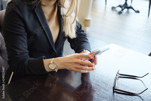 unrecognizable blonde business woman in suit with phone sitting at a table in a cafe, close up