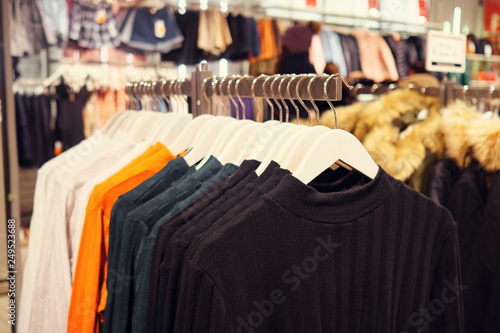 Rack with hangers of various colorful sweaters for sale in modern clothes store