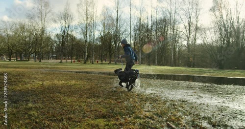 Happy boy and his young dog running through puddles in a park