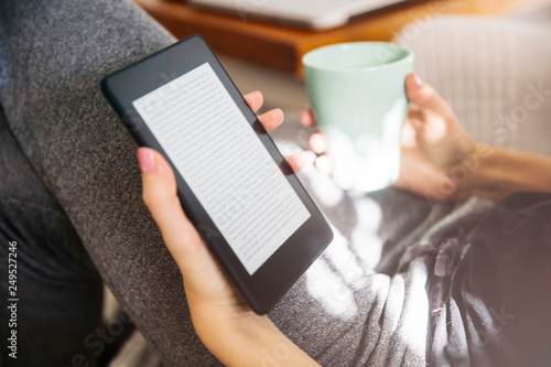 Fotografie Young woman drinking coffee and using an ebook reader