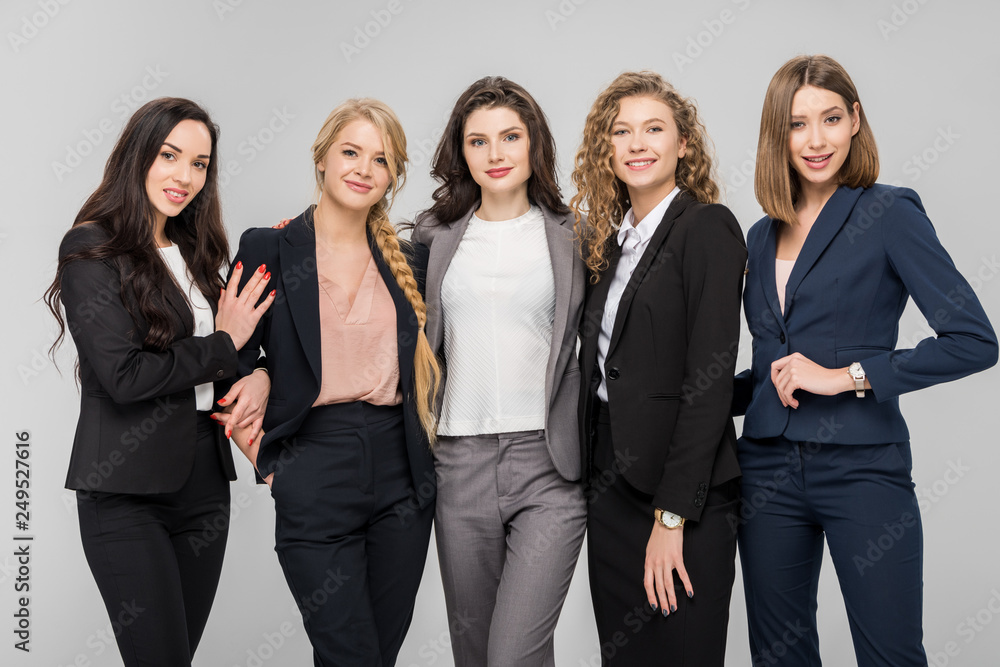 beautiful young businesswomen standing and smiling isolated on grey