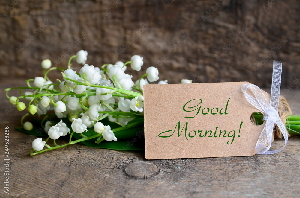 Naklejka premium Bouquet of fresh lily of the valley flowers and tag card with a Good Morning inscription on old wooden table.Beautiful spring still life concept.Selective focus.