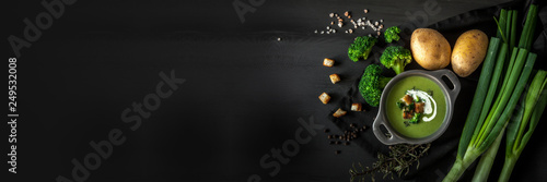 Spring detox broccoli green cream soup with potatoes and vegan cream in bowl on dark wooden board over black background, top view. Clean eating, dieting, vegan, vegetarian, healthy food concept