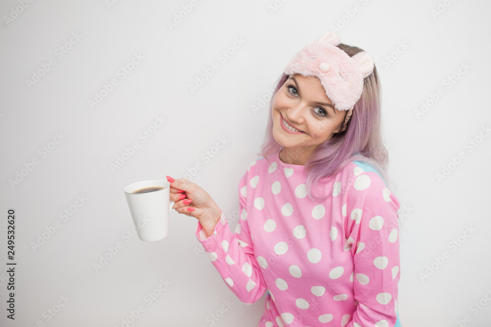Happy young woman drink morning coffee. Beautiful girl in pink pajamas and mask Happy young woman drink morning coffee. Beautiful girl in pink pajamas and mask