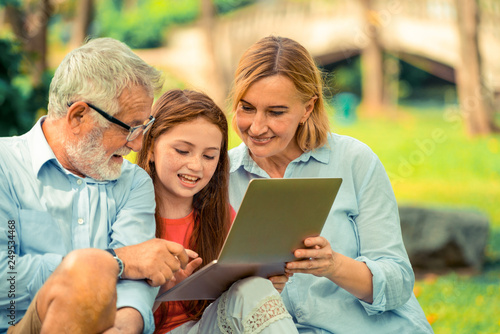 Happy family using laptop computer together in the garden park in summer. Kid education and family activities concept. photo