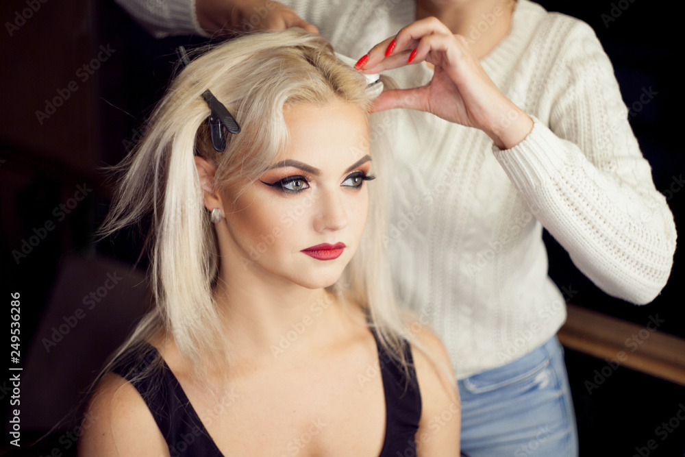 Fototapeta premium Beautiful young blonde. Makeup artist makes hair.