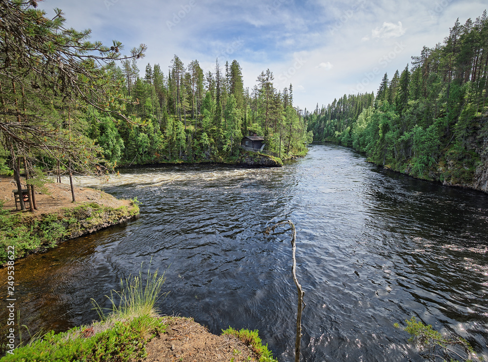 Oulanka river and the fast-moving rapids at the Oulanka National Park in Kuusamo, Finland. Green forest framing the flowing water. Finnish nature on a beautiful, sunny summer day perfect for hiking.