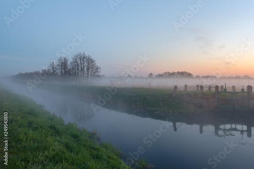 Mysterious foggy evening in a field near the river at the sunset time. Karwia village in Poland. photo