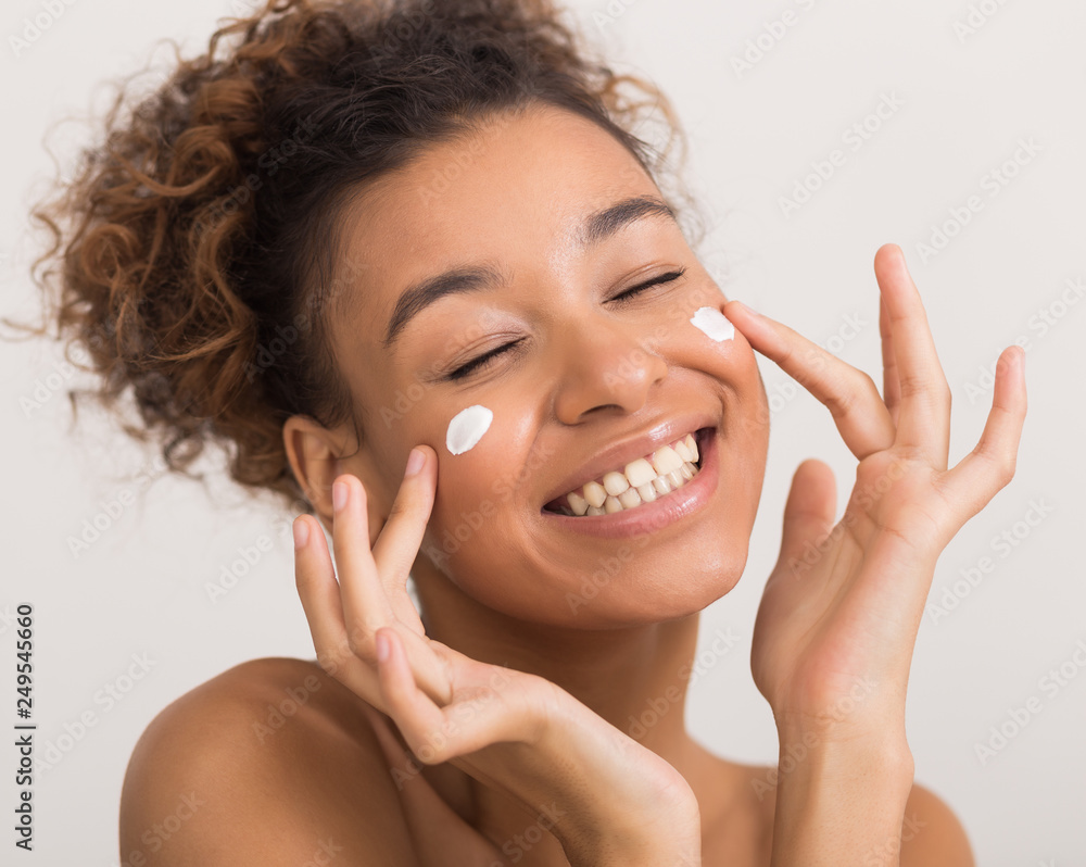 Happy african-american woman applying face cream, crop Happy african-american woman applying face cream, crop