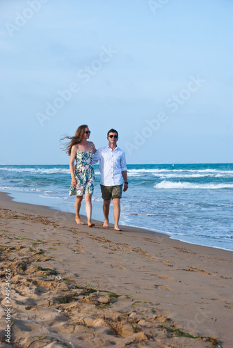 Beach couple walking on romantic travel honeymoon vacation summer holidays romance. Young happy lovers, Caucasian man and woman holding hands embracing outdoors.