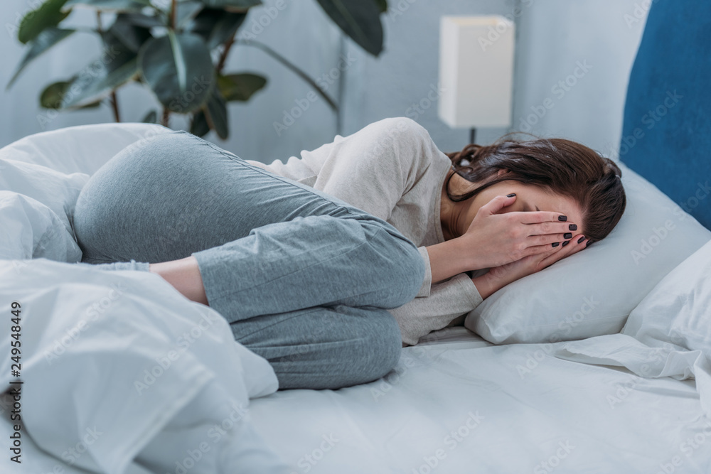 depressed woman lying in bed, crying and covering face with hands depressed woman lying in bed, crying and covering face with hands