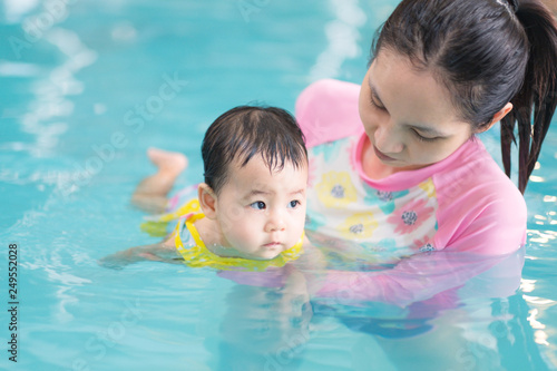 Mother and asian baby girl swimming in a pool, early development class for infants swimming. Baby swimming concept.