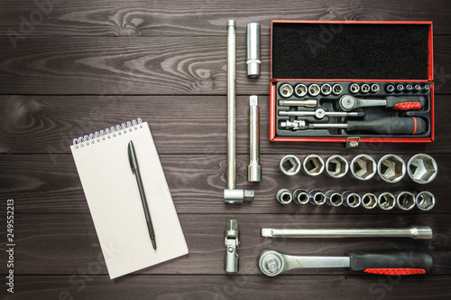 notebook and set of tools for an auto mechanic on a dark wooden workbench.