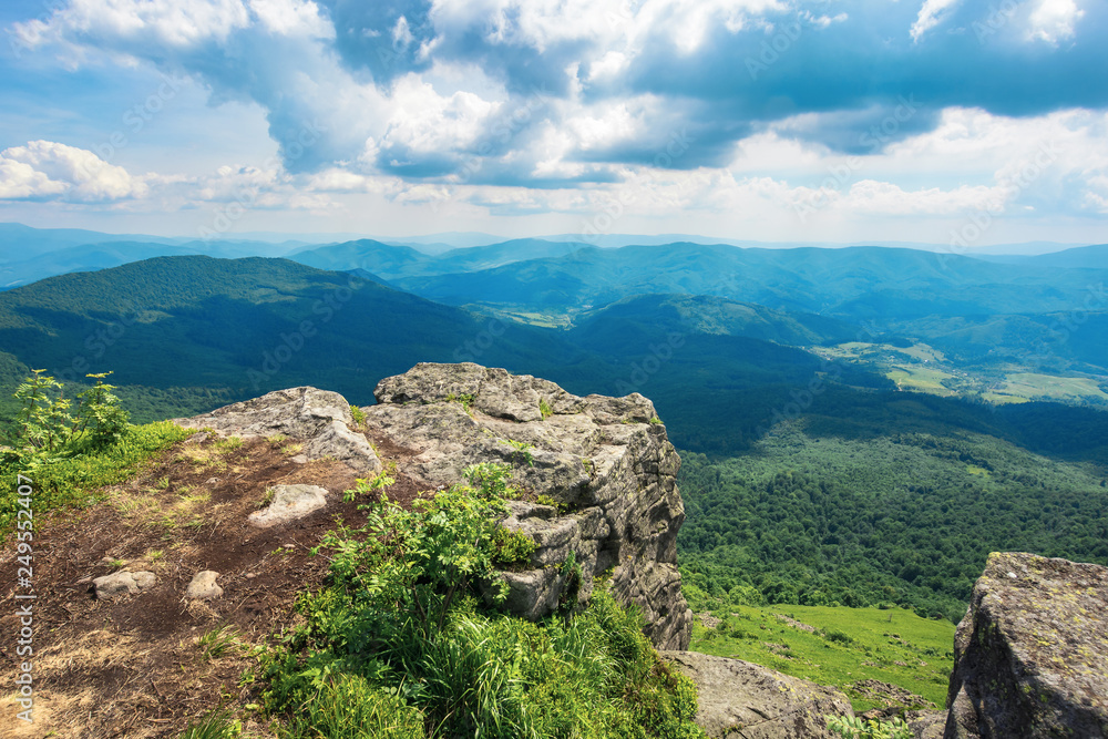 view from a rocky cliff in to the distant valley. beautiful summer landscape in mountains. huge ridge in the distance. view from above. cloudy weather