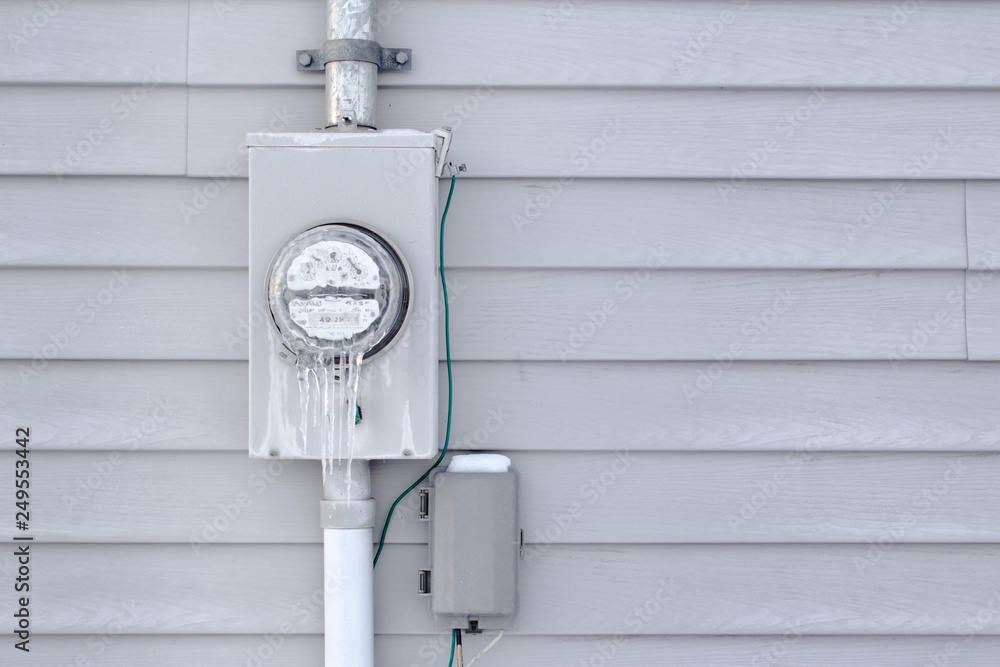Frozen electrical utility meter on house exterior siding. Stock Photo