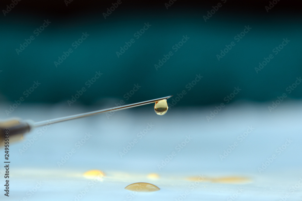 A drop of medicine hangs on a needle point of a syringe against a dark background. A drop of medicine hangs on a needle point of a syringe against a dark background.