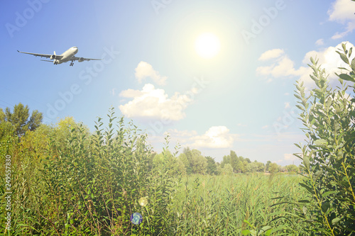 Plane in the sky with clouds and the sun bright over nature green.