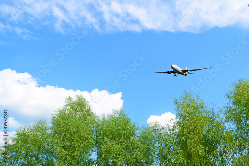 The plane flies in the sky over the green trees.