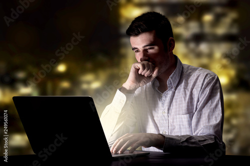 Young handsome businessman working late at night in the office with city lights in the background © ra2 studio