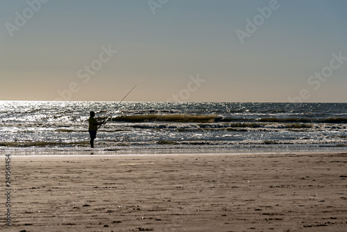 Silhouette of a man fishing alone on the beach with a view of the horizon