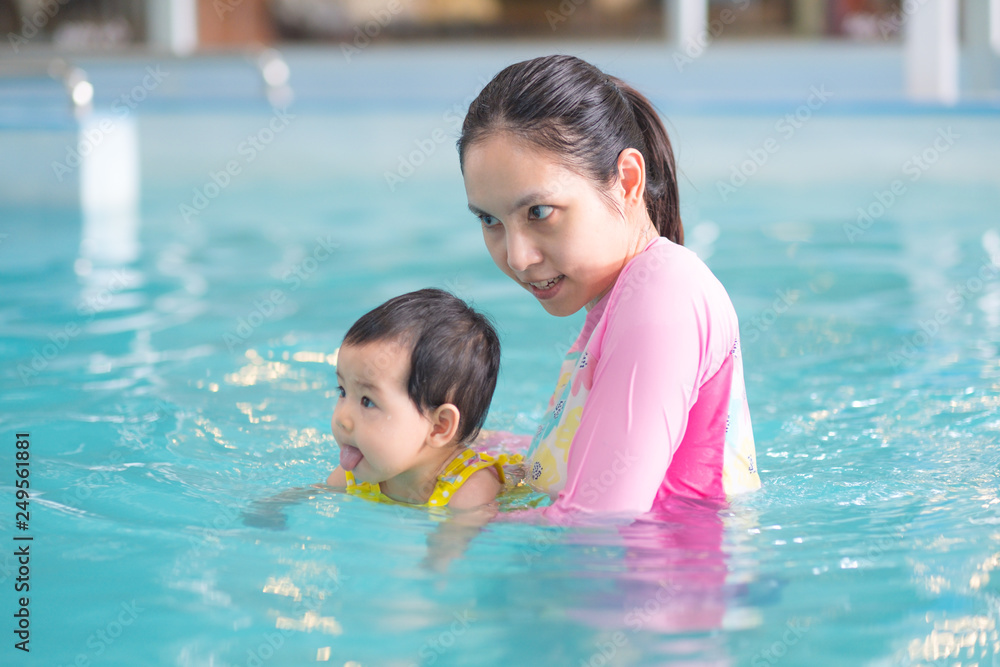 Mother and asian baby girl swimming in a pool, early development class for infants swimming. Baby swimming concept.