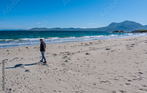 One man walking on the beach on a sunny day, showing hills and blue skies in the background. Taken on Renvyle beach along the Wild Atlantic Way in Ireland. photo