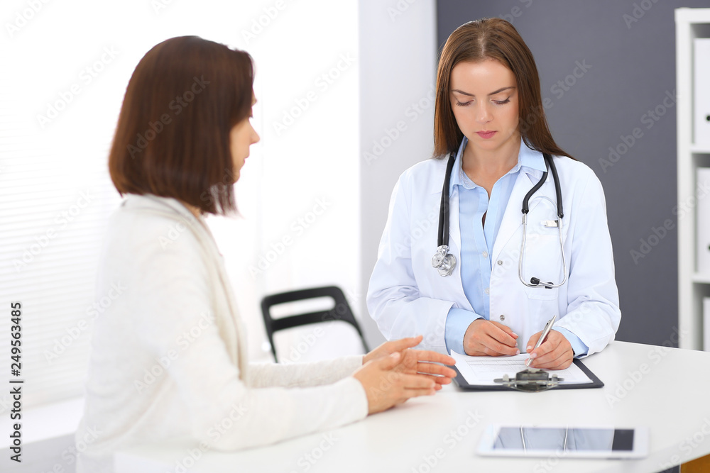Doctor and patient discussing something while standing near reception desk in emergency hospital. Physician at work in clinic. Medicine and health care concept Doctor and patient discussing something while standing near reception desk in emergency hospital. Physician at work in clinic. Medicine and health care concept