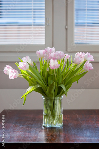 A fresh and clean home office with soft pink tulip flowers on a dark wooden table for Valentine's Day celebration. Airy Scandinavian/Nordic interior style on a media office in Finland.