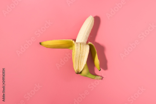 Fresh peeled banana on pink background with contrast shadows, flat lay