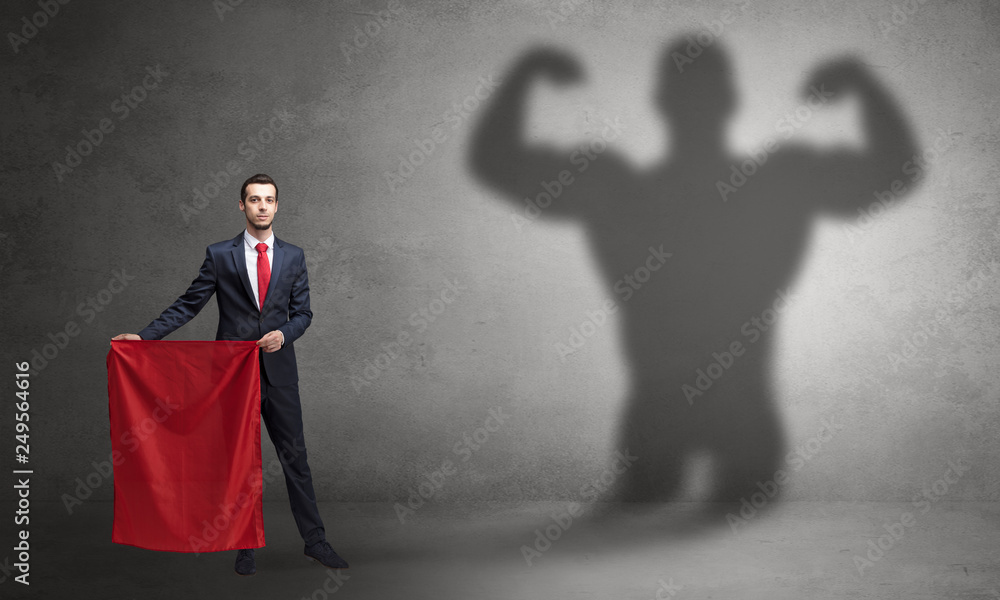 Obraz premium Businessman standing with red cloth on his hand and strong hero shadow on the background 