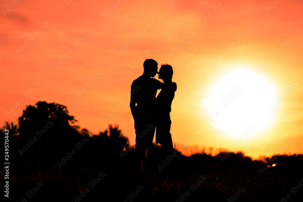 Young man hugging his girlfriend on a sunset sky background