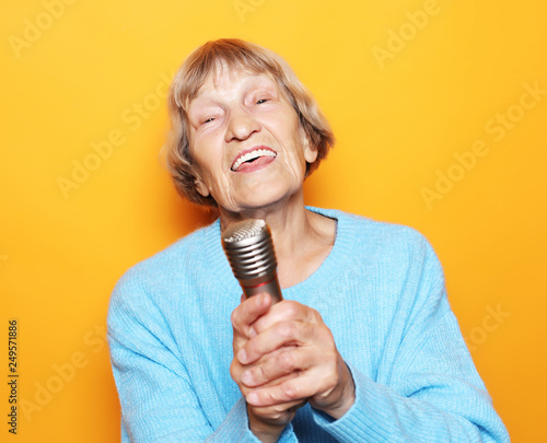 lifestyle and people concept: Happy old senior woman singing with microphone, having fun, expressing musical talent