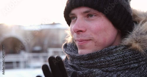 Handsome young man exhaling warm air from mouth and rubbing hands on a cold winter day