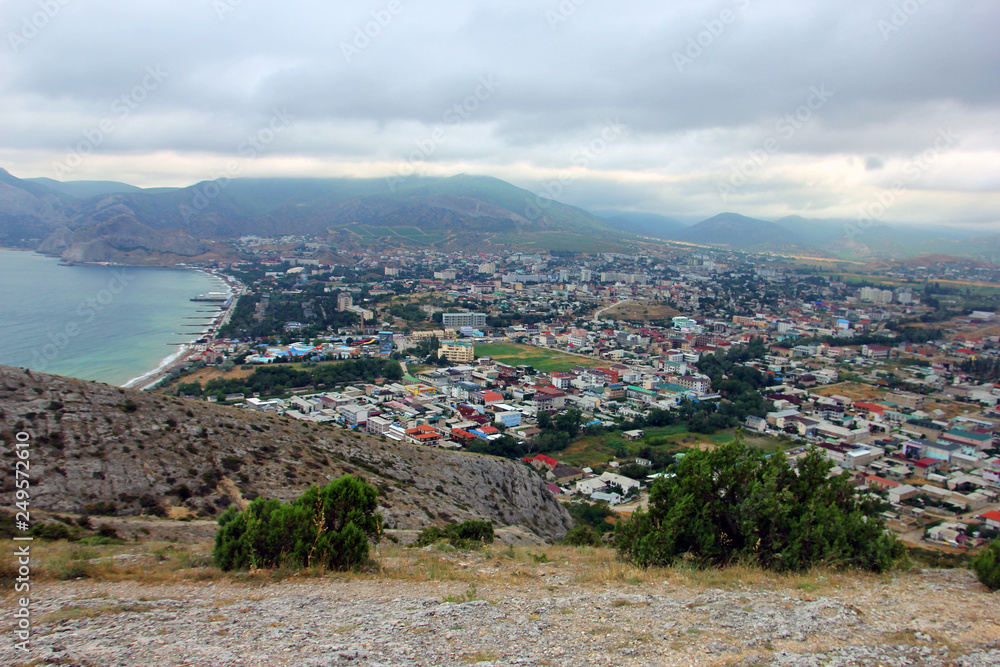 view from the top of a rocky mountain to the sea Bay and small town Sudak in valley and winding steppe coast in Crimea