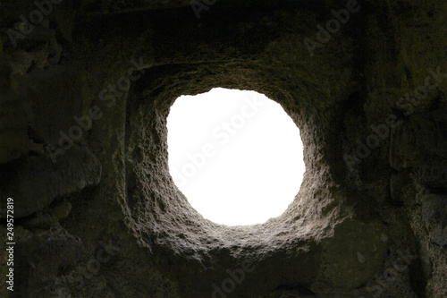round uneven hole in dark stone wall with white background. loophole in the fortress wall
