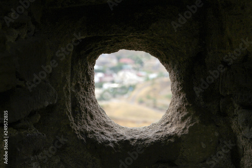 round uneven hole in dark stone wall with white background. loophole in the fortress wall