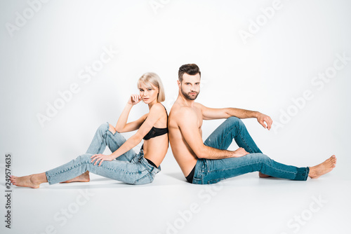 beautiful girlfriend and handsome boyfriend in underwear and jeans sitting back to back on grey