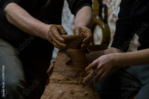 A raw clay pot in the hands of a Potter. Master teach to child the mold with spirituality. Craftsman artist making craft, pottery, sculptor from fresh wet clay on pottery wheel, selected focus.