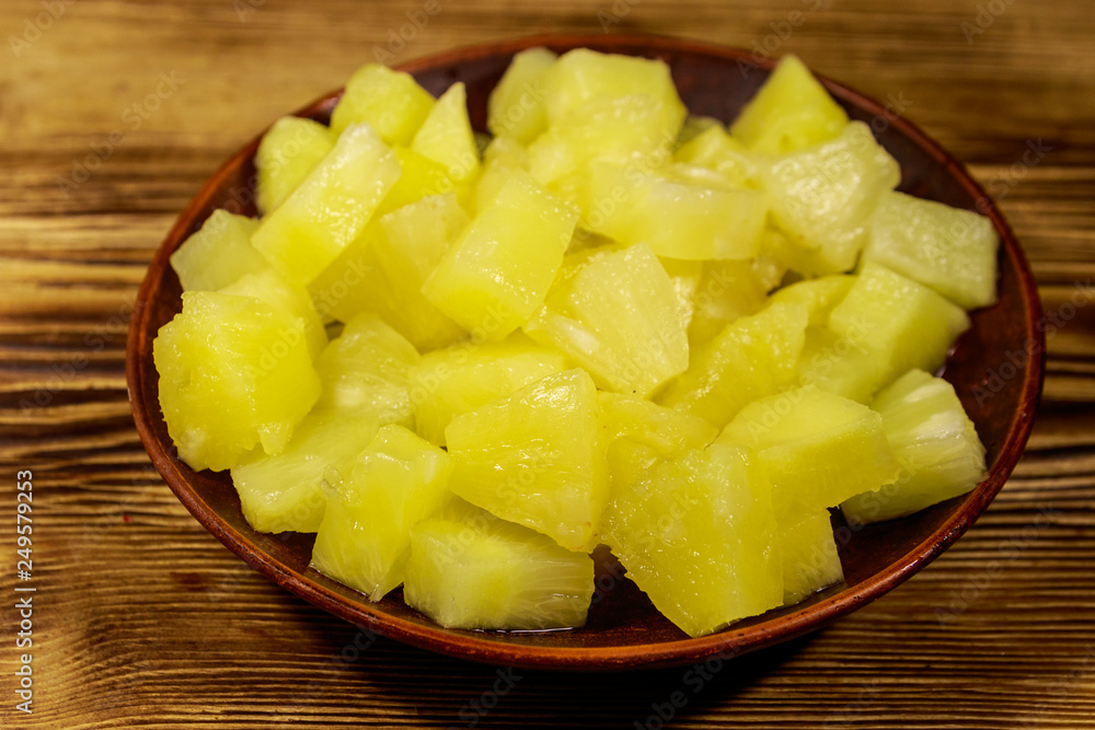 Canned pineapple pieces in ceramic plate on wooden table Canned pineapple pieces in ceramic plate on wooden table