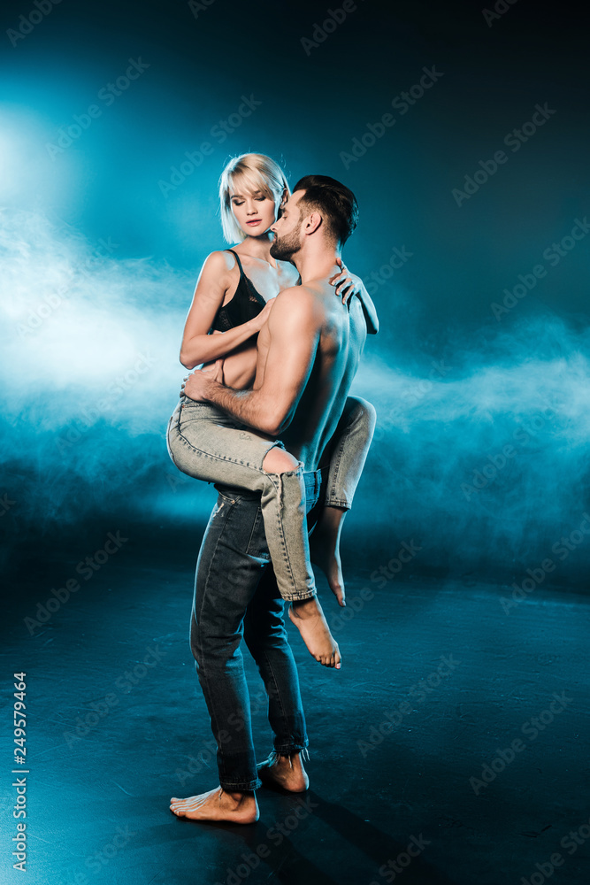 handsome seductive man holding blonde girlfriend on blue smoky background