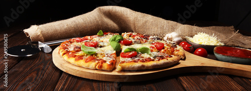 Vegetarian Italian pizza with melted cheese, red tomatoes and green basil on a table decorated by cheese, tomato and cherry tomatoes