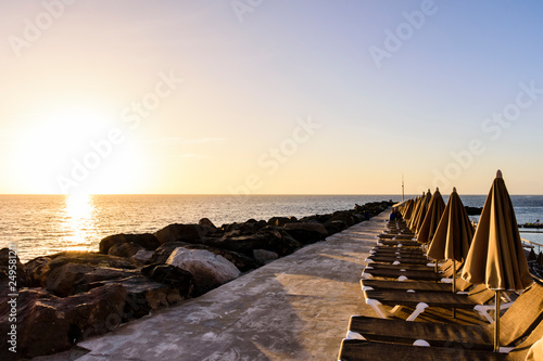 beach lounge chairs and umbrellas in front of the sun during sunset photo