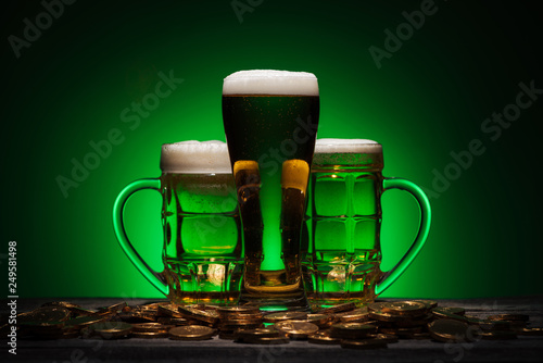 glasses of beer standing near golden coins on st patricks day on green background