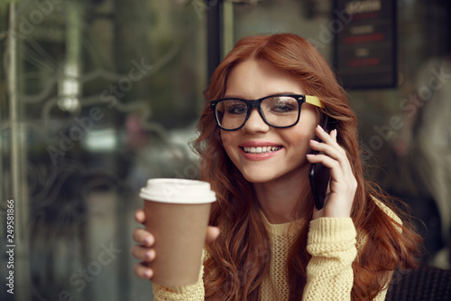 Cheerful pretty girl with hot drink talking on cellphone