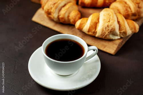 coffee and croissants on wooden cutting board, on the background concrete