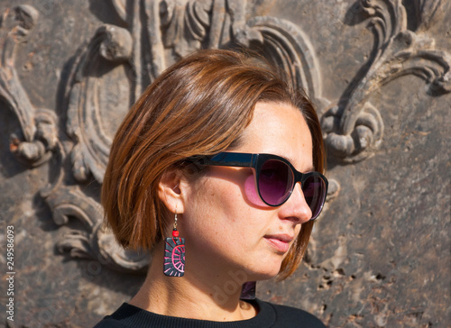 Attractive woman in bright tribal earrings and sunglasses near vintage wall in baroco style. photo