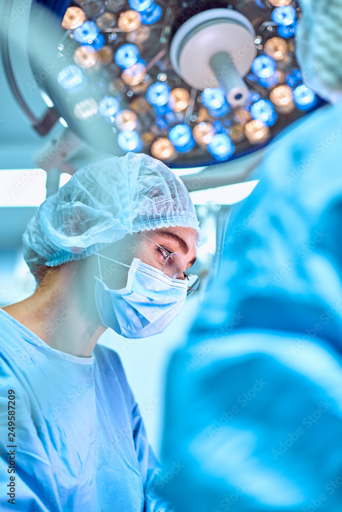 Close up portrait of young female surgeon doctor wearing protective mask and hat during the operation. Healthcare, medical education, surgery concept Close up portrait of young female surgeon doctor wearing protective mask and hat during the operation. Healthcare, medical education, surgery concept