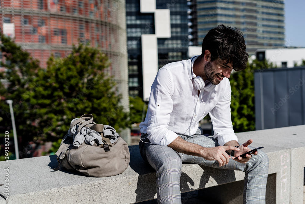 Smiling young man sitting on a bench outdoors using cell phone Smiling young man sitting on a bench outdoors using cell phone