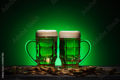 glasses of alcohol beer standing near golden coins on st patricks day on green background